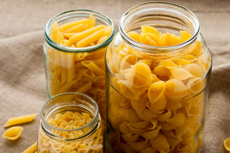 Different types of yellow macaroni pasta in glass bowl on hessian fabric cloth backgroundの写真素材