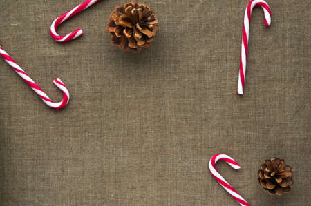 Christmas decorations: top view composition of candy canes and cones on linen fabric background