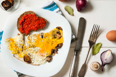 Top view of plate of fried eggs and mushrooms with bread on white wooden table surfaceの写真素材