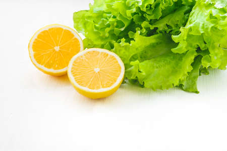 Yellow lemon half and green leaf lettuce on white wooden table and partly isolated