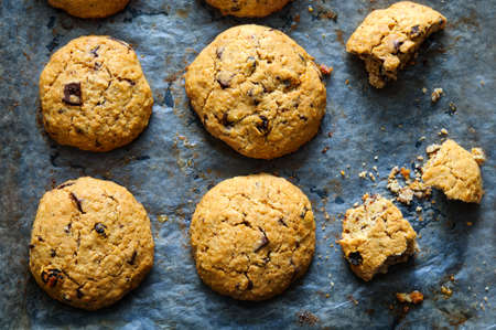 Freshly baked oat raisin cookies on dark baking paper. Top flat view with natural directional...