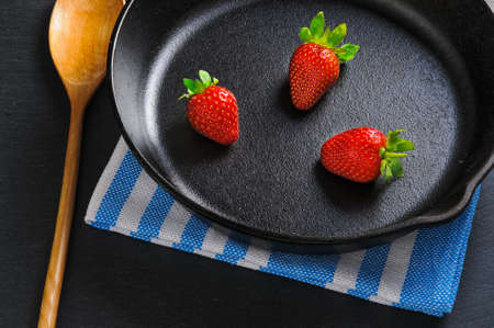 Three fresh red strawberries on black cast-iron pan served with wooden spoon and napkinの写真素材