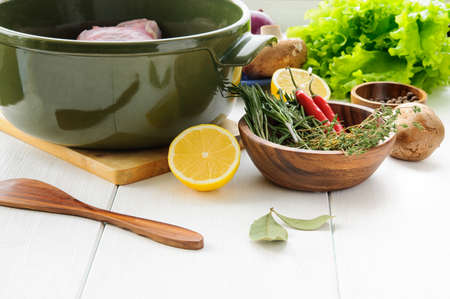 Raw rabbit meat with vegetables and herbs  in round ceramic pot on white wooden table surface