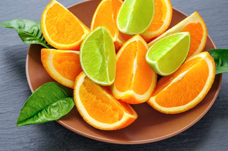 Orange and lime sliced segments  with green leaves on brown plate, black slate stoneの写真素材