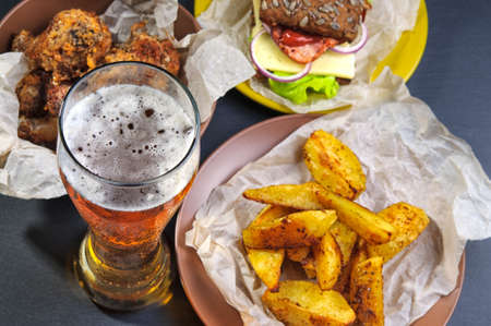 Top view of glass of beer, fries, sandwich and chicken legs on black slate stoneの写真素材