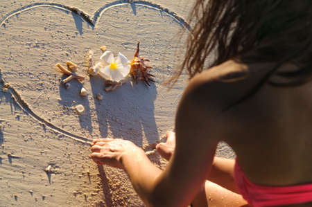 Girl at beach drawing heart on sand at sunsetの写真素材