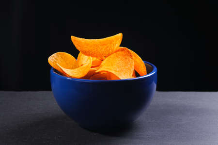 Potato chips in bowl on slate stone isolated on black