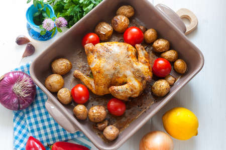 Roasted small chicken with potato and tomato in ceramic dish, top viewの写真素材
