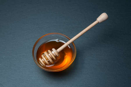 Small glass bowl of natural honey with stick. On the black stone rustic table.の写真素材