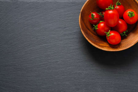 Cherry tomatoes in wooden bowl on black stone surface. Top view with copy spaceの写真素材