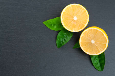 Freshly cut half lemons with leaves on black stone. Copy spaceの写真素材