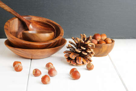 Wooden theme: hazelnuts, pinecone, utensil on white tableの写真素材
