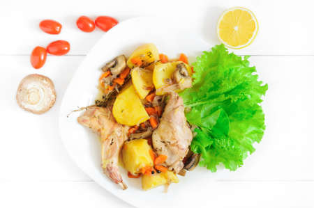 Top flat view of roasted rabbit meat with vegetables on white wooden table surfaceの写真素材