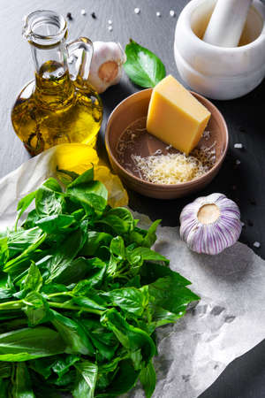 Homemade pesto ingredients: basil, olive oil, garlic and cheese on black slate stone surfaceの写真素材