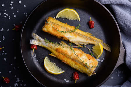 Top view of fried smelts on frying pan with lemon