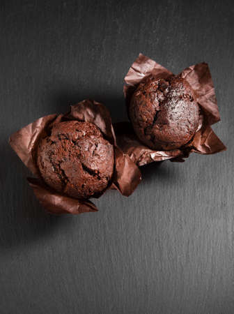 Two chocolate muffins in baked paper on black stone backgroundの写真素材