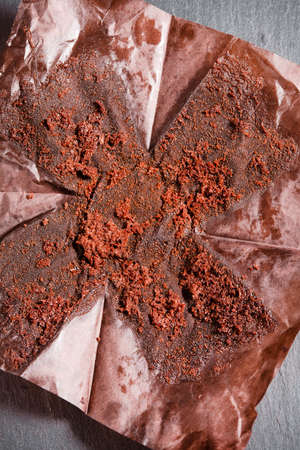 Crumpled baking paper after chocolate brownie close-up on black slate stone. Top flat view....