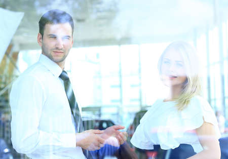 Two cheerful smiling young businesspeople talking at the office. View through windowの写真素材