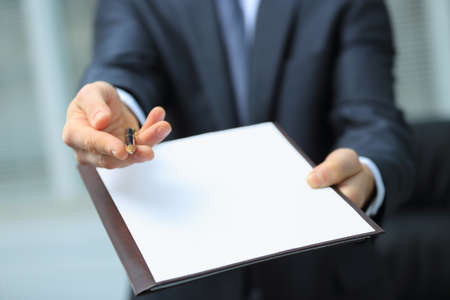 Businessman giving pen for your signature on clipboardの写真素材