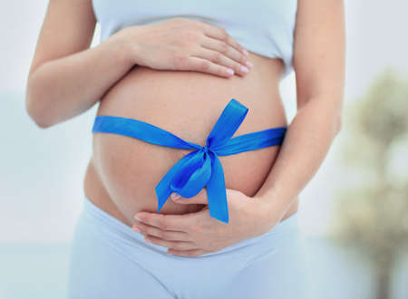 woman holding hands on her baby bump, tied with a blue bowの写真素材