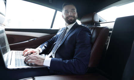 businessman with laptop sitting in the back seat of a car