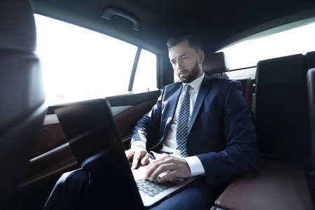 businessman sitting in the back-seat of a car, using his laptopの写真素材