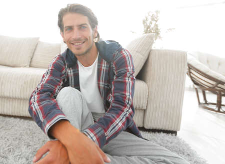confident guy sitting on the carpet in a cozy living room.の写真素材