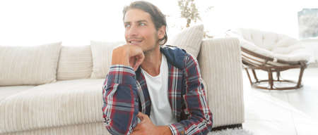 close-up of a dreaming guy sitting on a carpet in a cozy living roomの写真素材