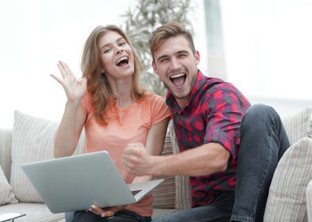young couple rejoices,sitting on the couch in front of the open laptopの写真素材