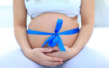 closeup of a pregnant woman tying a blue ribbon on her belly. the concept of health.の写真素材