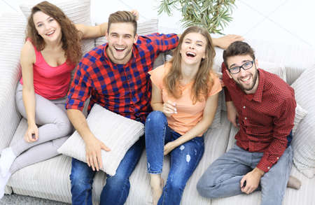 four happy friends laughing while sitting on the couchの写真素材