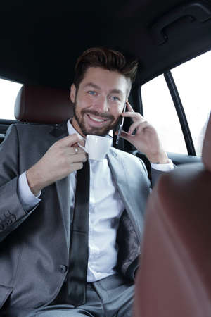 businessman sitting in car with cup and smartphone