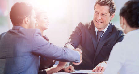 Mature businessman shaking hands to seal a deal with his partner and colleagues in a modern officeの写真素材