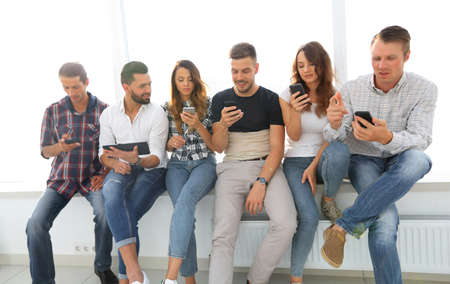 beautiful young people in casual clothes using gadgets while sitting together on the window sill