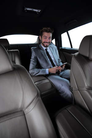 man in suit sitting in car and reading messages on smartphone