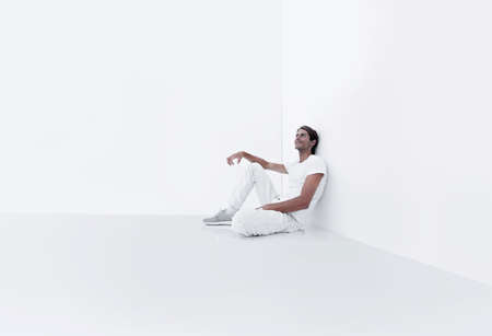 dreamy young man sitting beside a white wall.の写真素材