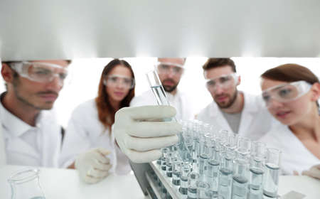 background image is a group of microbiologists studying the liquid in the glass tube.