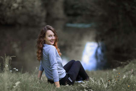 young woman sitting near the riverの写真素材