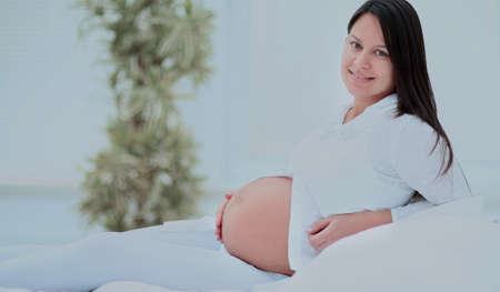 Pregnant woman lying on the bed, smiling and looking into the cameraの写真素材