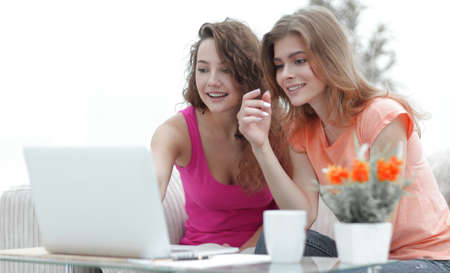 two young women discuss the video with laptop sitting at a coffee tableの写真素材