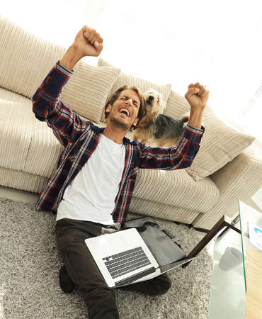 happy guy with laptop jubilant in spacious living room.の写真素材
