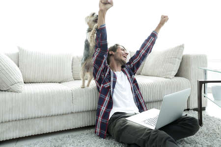 happy guy exults with his dog sitting near the sofa in the living room.の写真素材