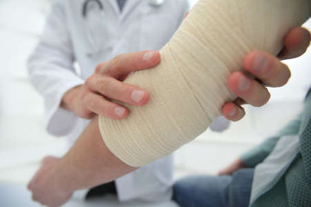 Orthopedist applying bandage onto patients hand in clinic