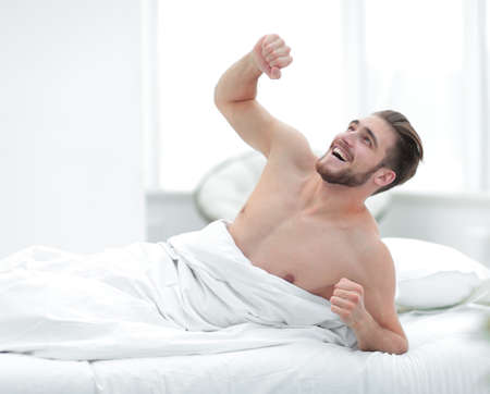 smiling man waking up in a cosy bedroomの写真素材