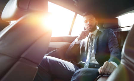 businessman talking on the phone while sitting in the back seat of his carの写真素材