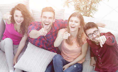 group of laughing friends sitting on sofa and showing forefingerの写真素材