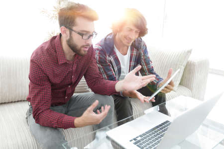 two guys sitting on the couch and looking at the laptop screen.