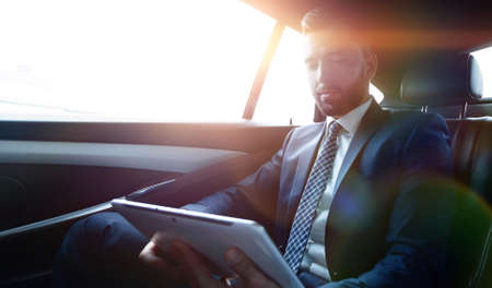 businessman working in the back seat of a car and using a tabletの写真素材