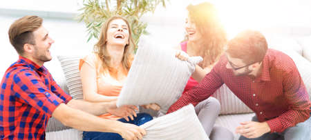 cheerful friends playing with the pillows sitting on the couchの写真素材