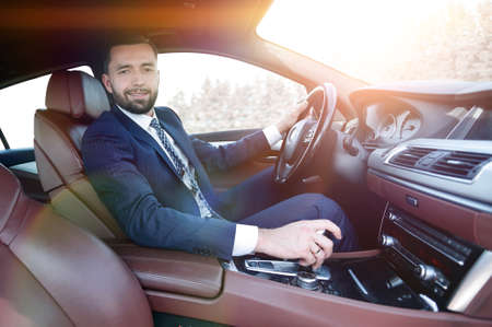 View from the side confident businessman sits at the wheel of aの写真素材